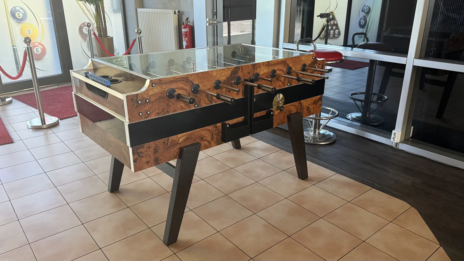 Kicker aus Holz mit Glasplatte im gefliesten Eingangsbereich der Sportsbar Voerde, dahinter Fenster mit Billardkugel-Motiven
