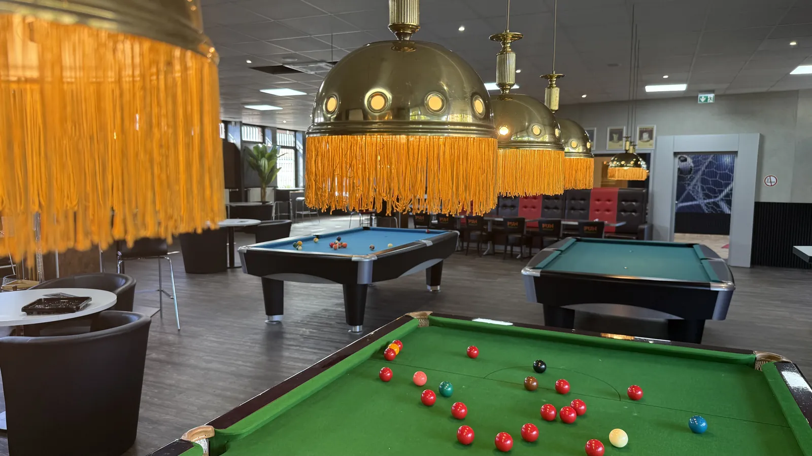 Blick über den Snookertisch mit grünem Tuch auf die Pooltische unter goldenen Fransenlampen